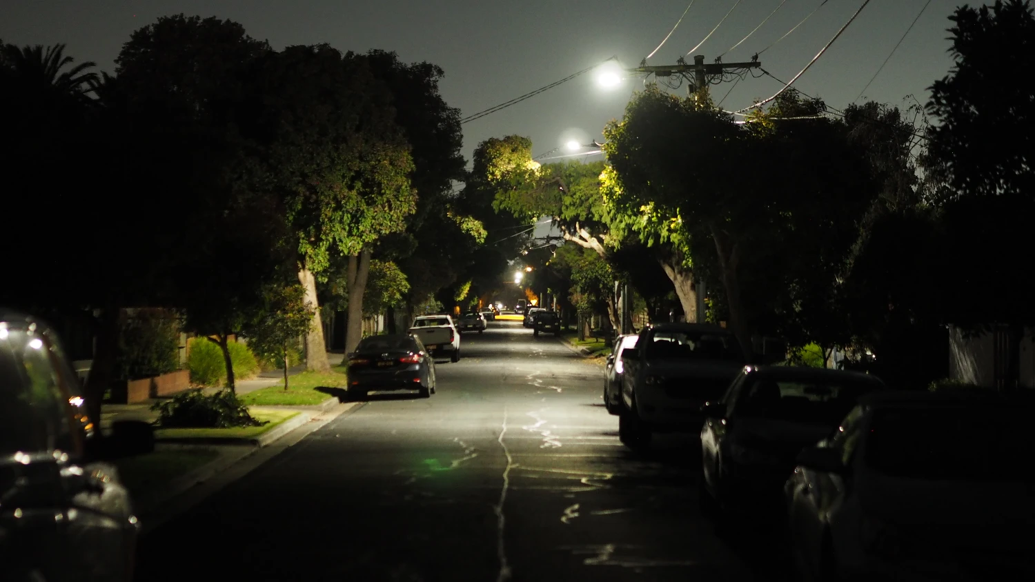 An empty road at night with cars parked on either side.