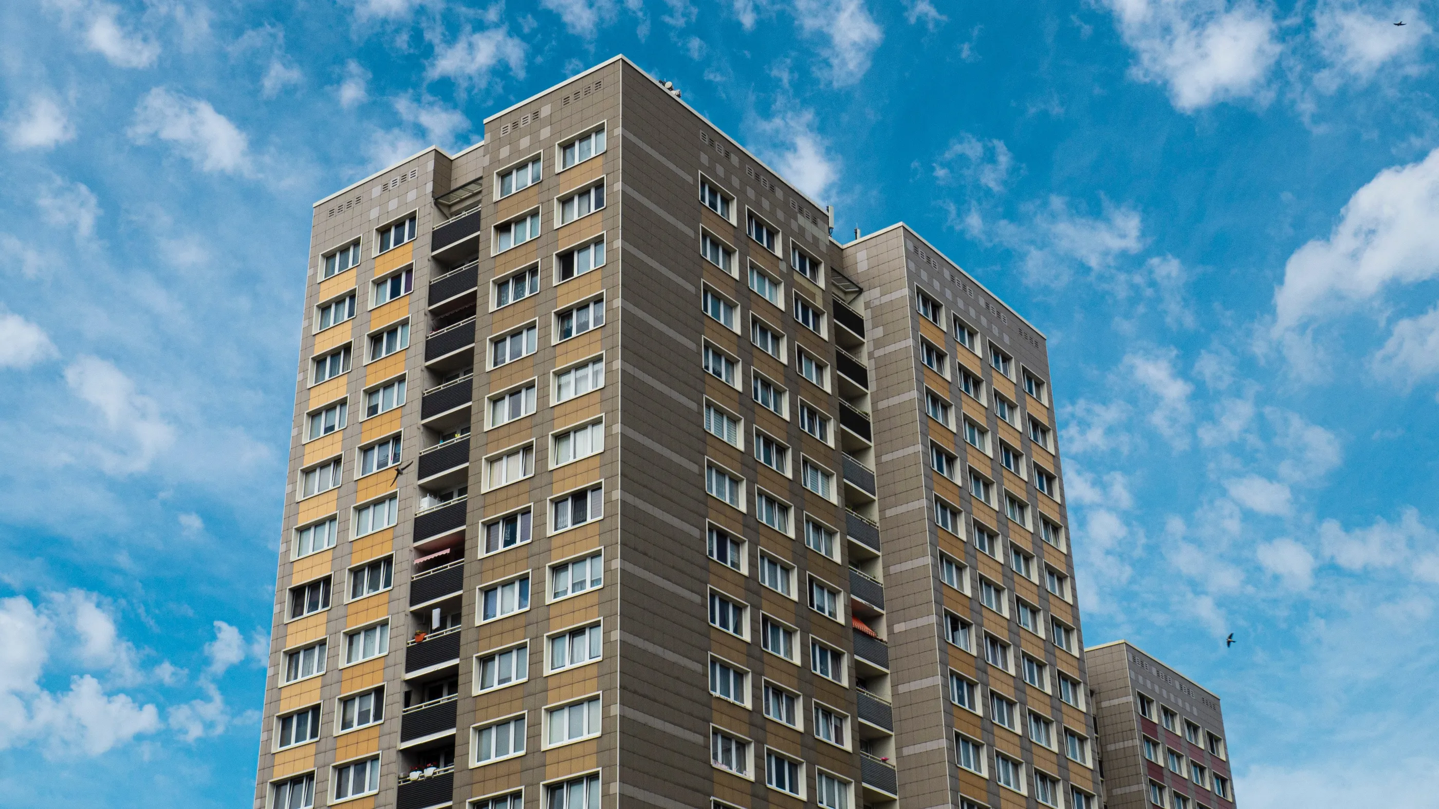 The top of a grey apartment block, against the backdrop of blue sky.
