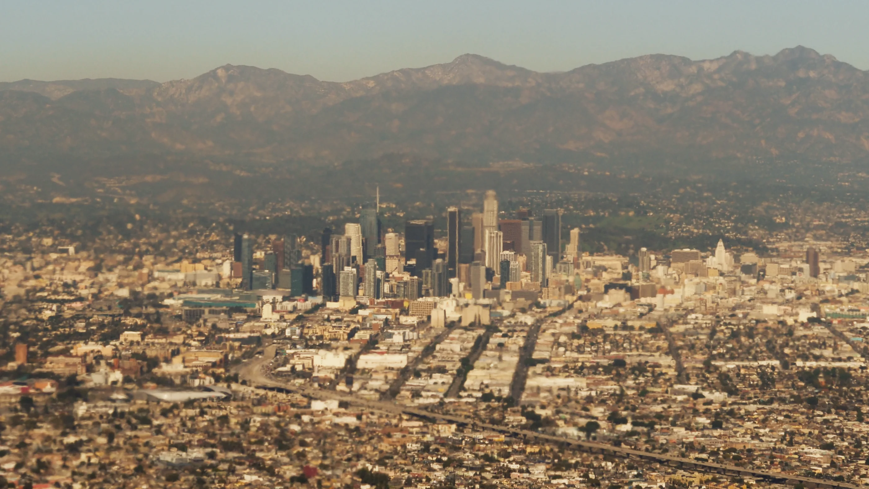 A picture take from the air, showing the high-rises of central Los Angeles in the from the mountains of the Angeles National Forest in the background.
