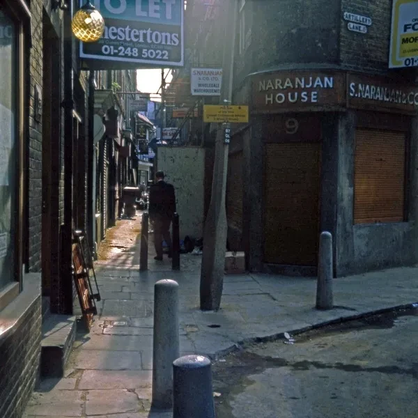 A narrow alleway, nestled in between brick houses. A man is seen walking down the alleyway, way from the camera.