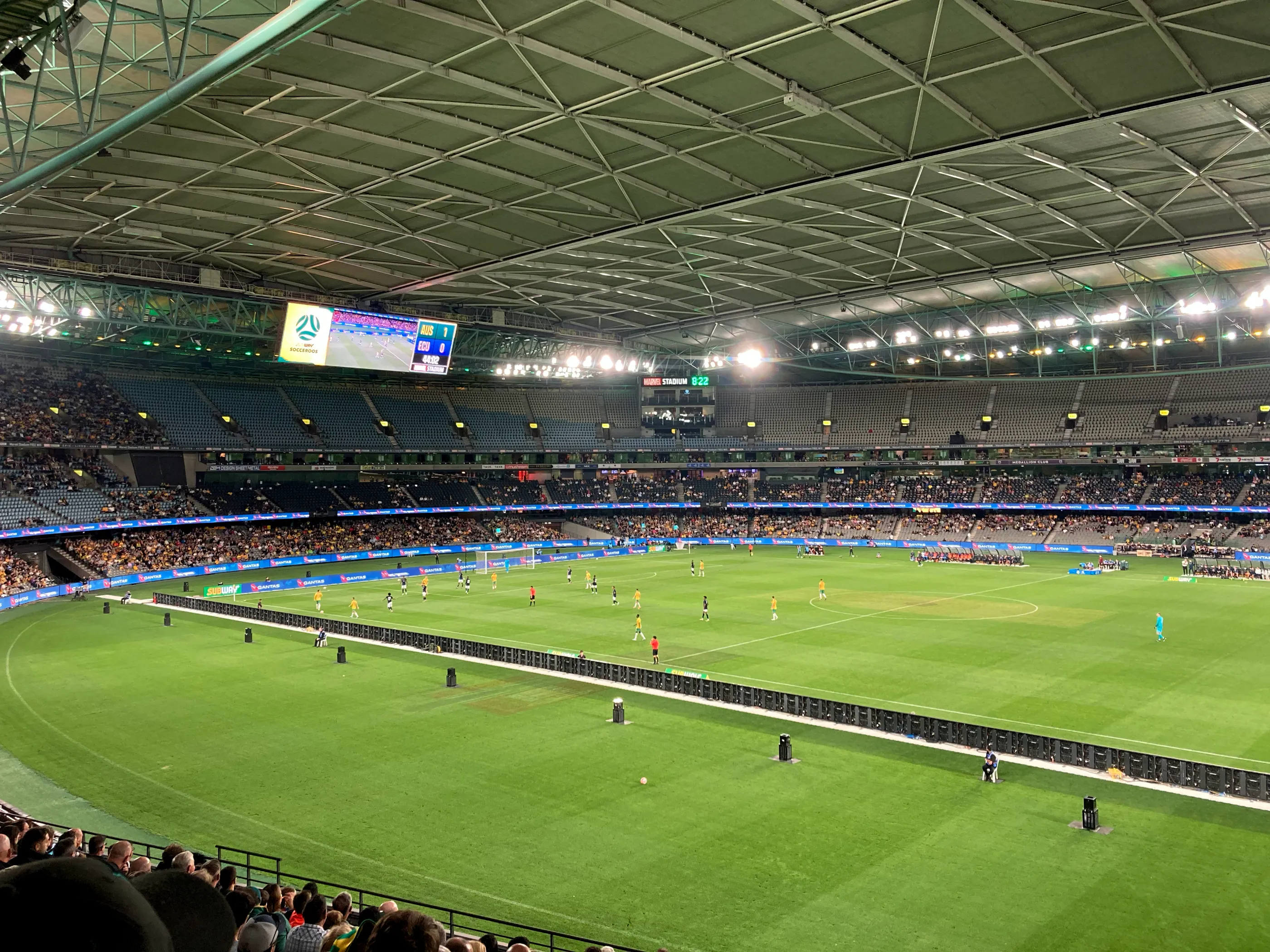 Panoramic view of a football match at Marvel Stadium in Melbourne. The photo is take from the corner, the play happens in the opposite half, the stands are half empty.