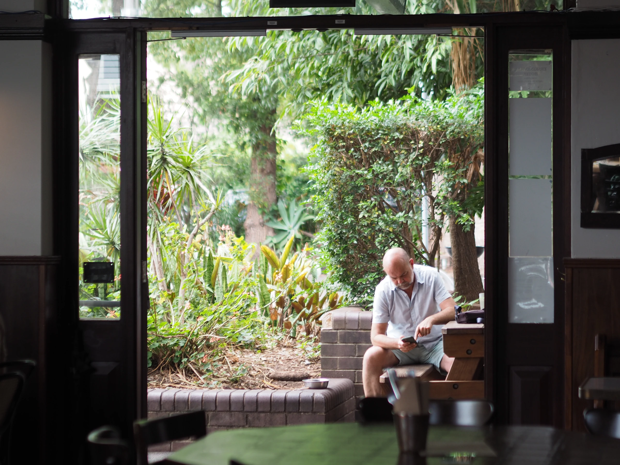 A man sitting outside a pub, seen from inside the pub.